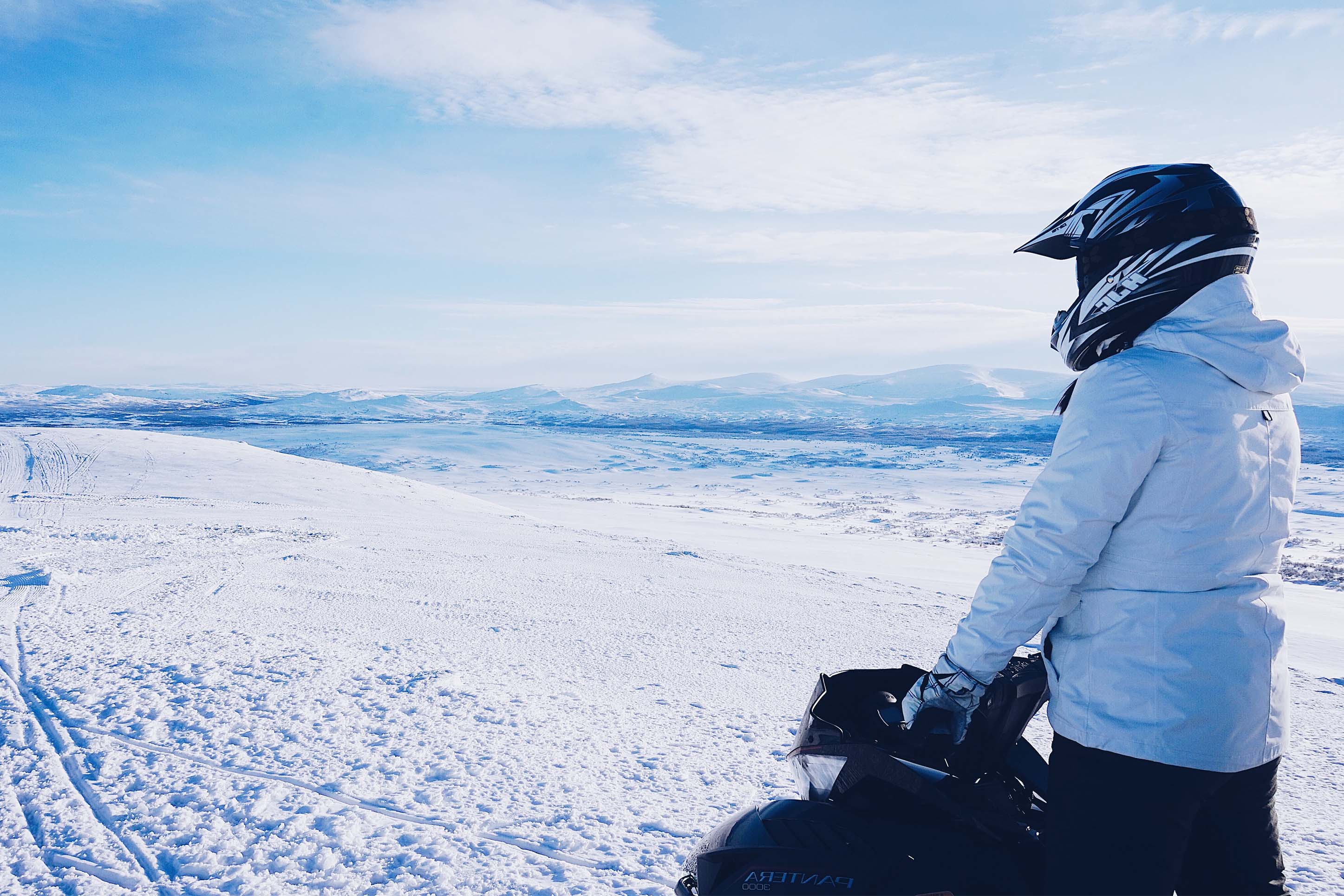 woman overlooking a snowy field while on her snowmobile