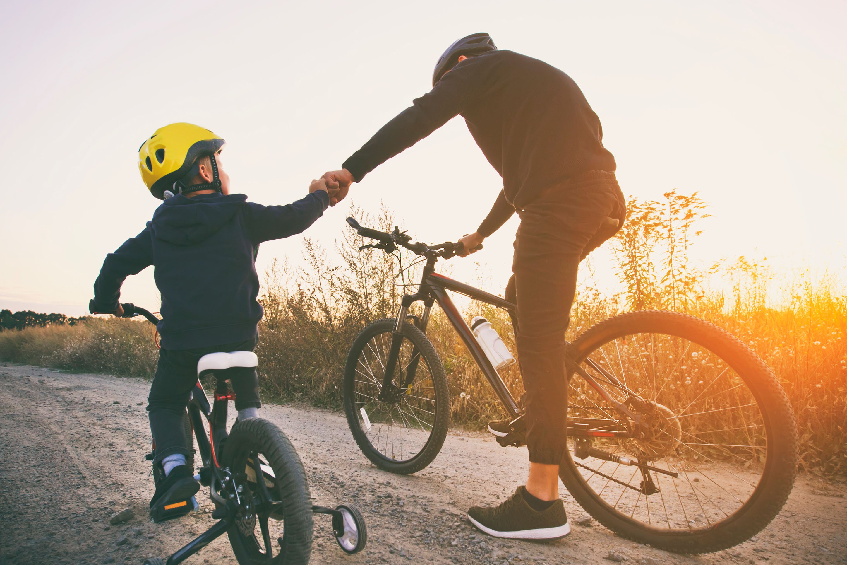 Dad and son holding hands and biking. 