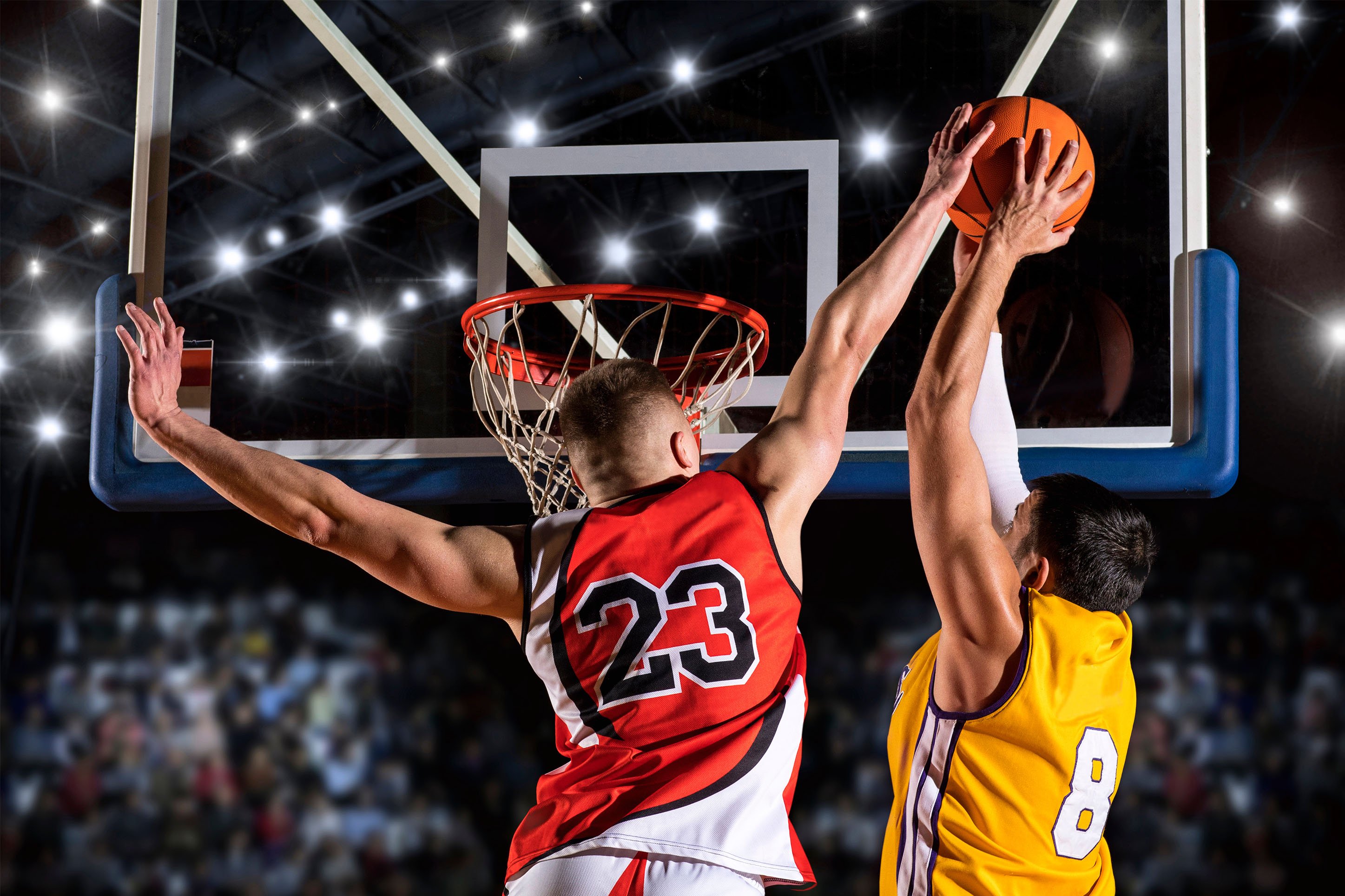 Two basketball players, one trying to dunk, one trying to block. 