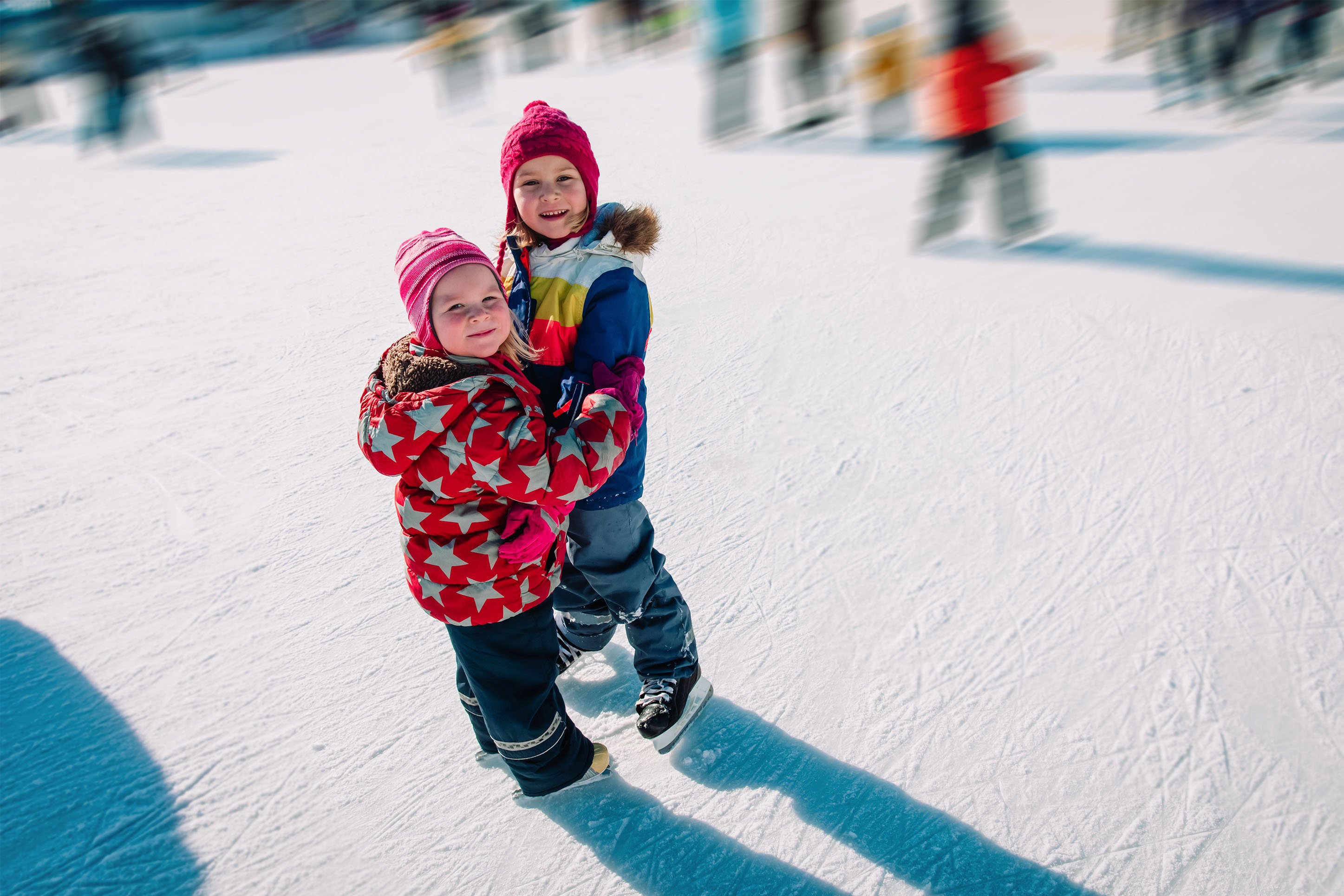 Two kids holding on to each other ice skating. 