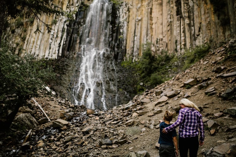 A mother and sun admiring a waterfall while on a hike
