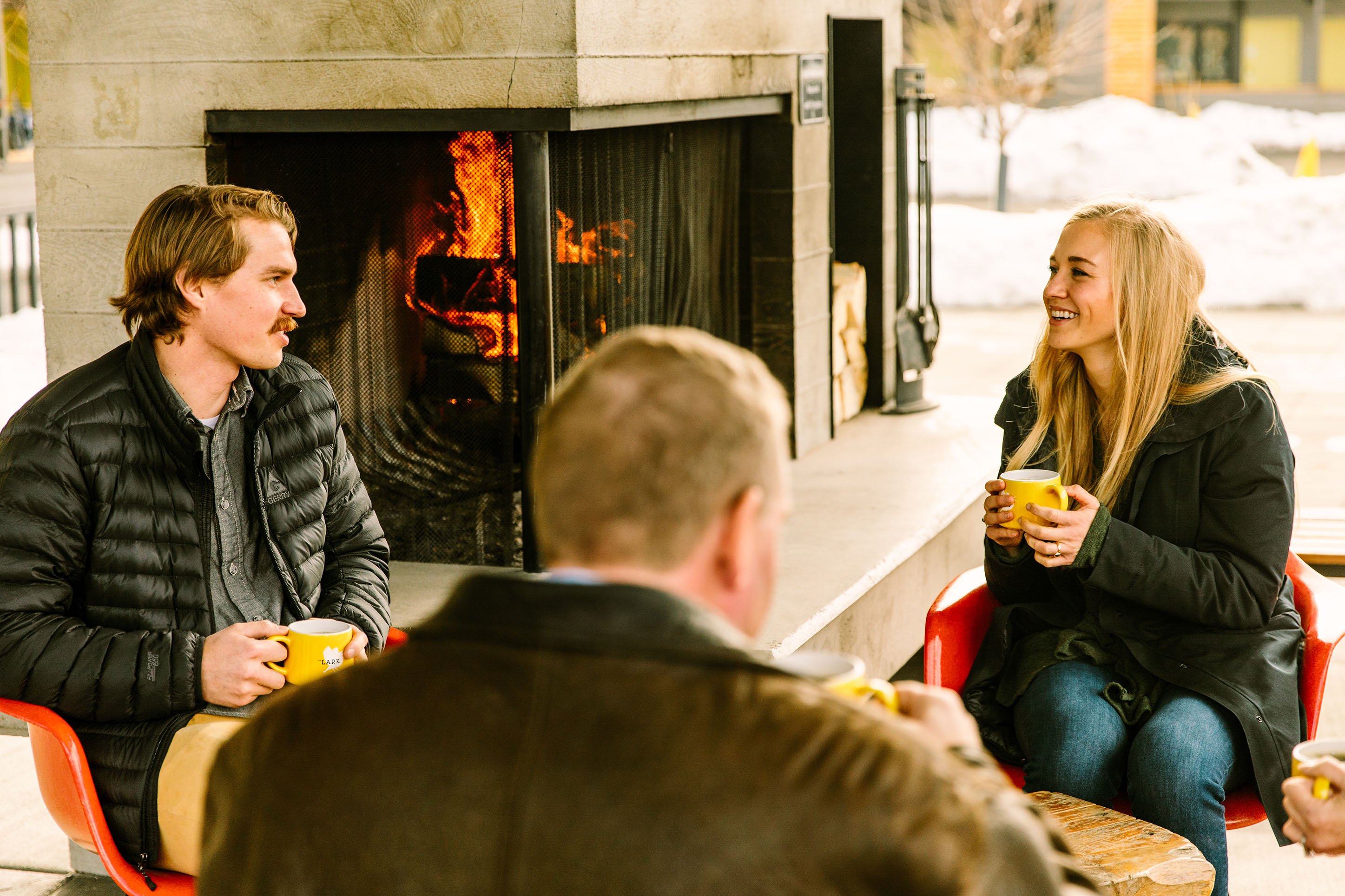 Friends gathering for coffee around a fireplace.