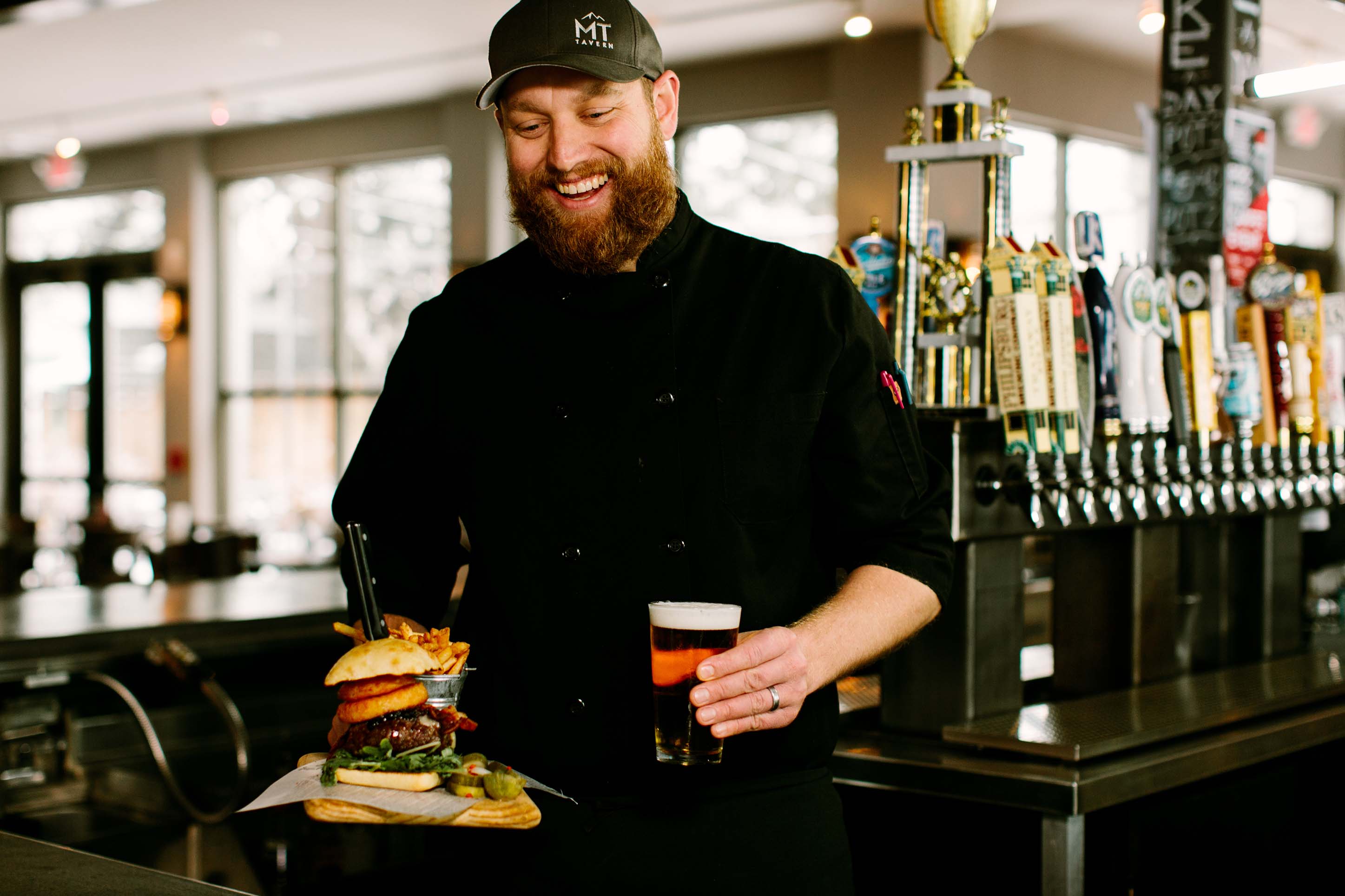 Man smiling serving a burger and a beer. 