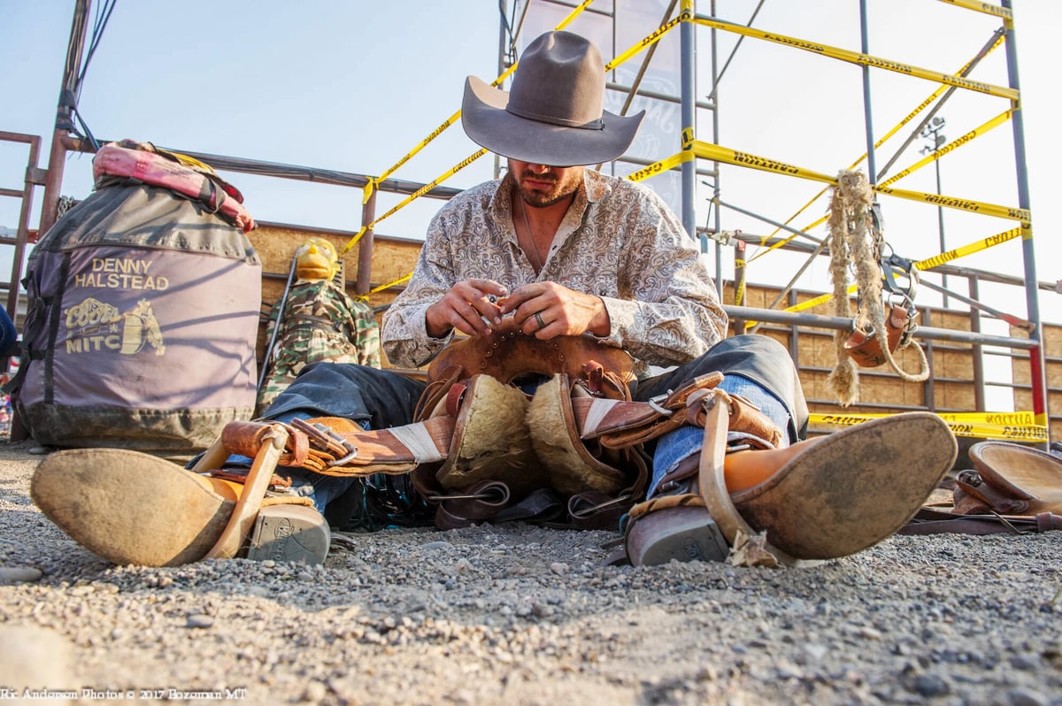 Cowboy sitting on the floor of a rodeo arena and prepping a saddle