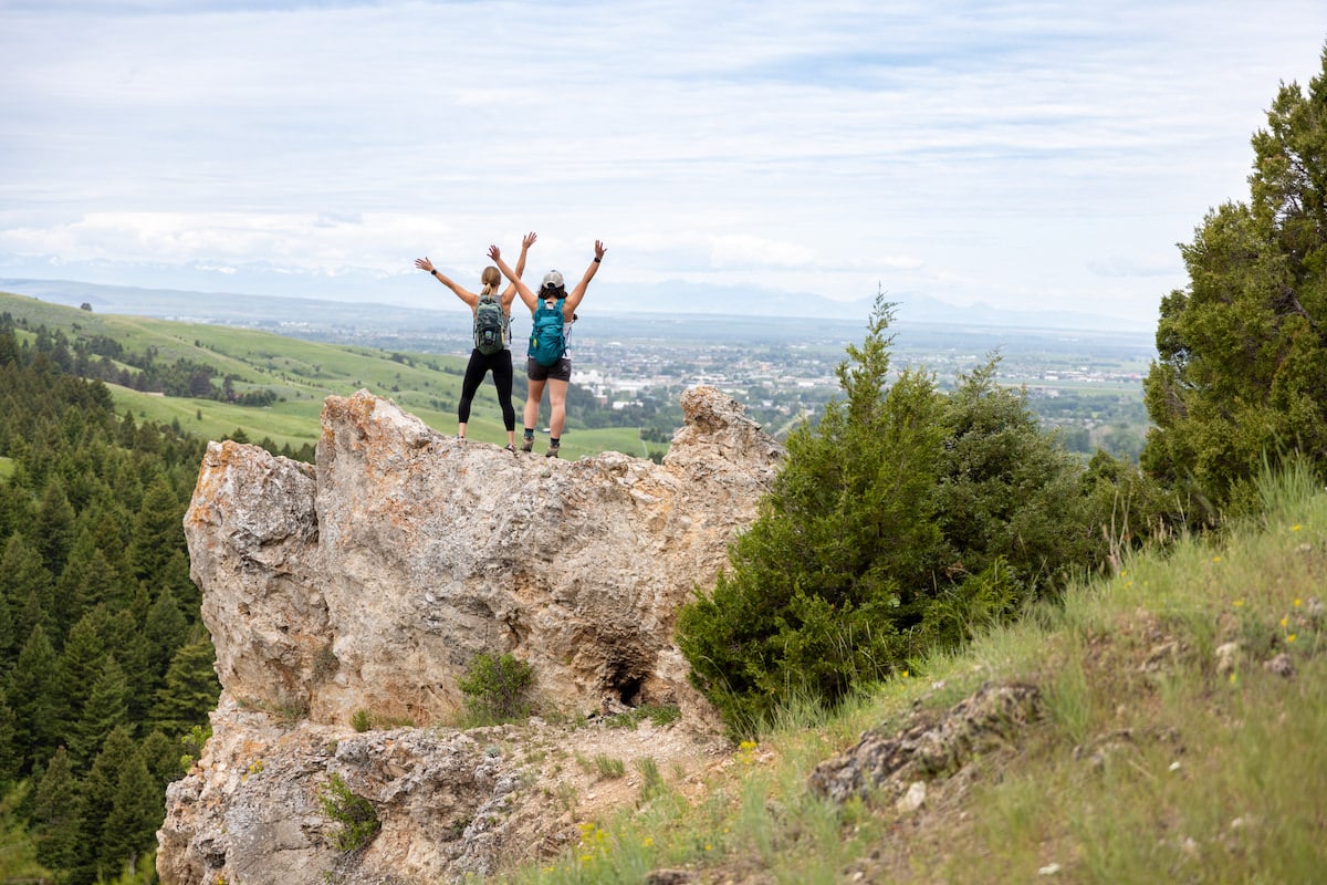 Two women holding their arms up high on the M Trail in Bozeman, Montana.